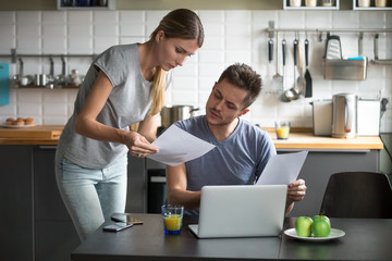 Serious millennial couple worried about high utility bills or rent payment reading papers in...