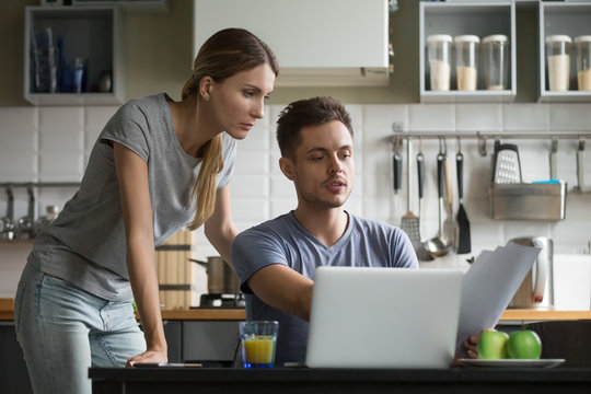 Young serious couple discussing papers with laptop, man and woman roommates or husband and wife checking rent or domestic bills to pay online, planning budget or analyzing financial expenses together