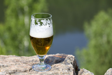 Wineglass of beer is stand on a rock above the river