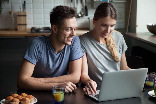 Young couple using laptop together having breakfast at home, man and woman communicating in social network, searching for new sale offers or shopping in online computer application in the kitchen