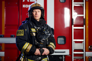 Photo of fireman wearing helmet with gas mask on background of fire engine with stair at station
