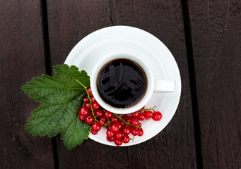 white coffee cup with tea, which on a saucer lay the juicy berries of red currant on a green leaf