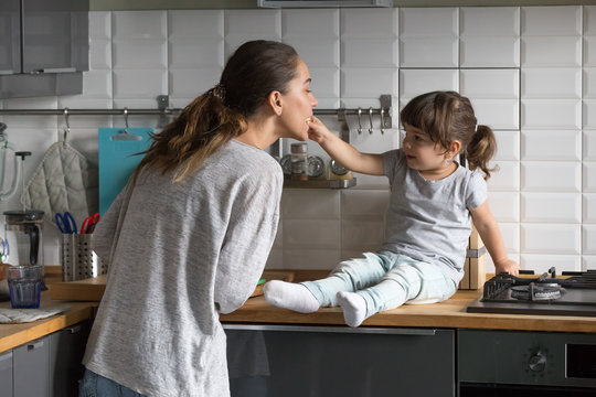 Little Daughter Feeding Mother Having Fun In The Kitchen At Home, Cute Girl Helping Young Single Mom Or Sister Playing While Cooking Together, Mommy And Kid Lifestyle, Funny Family Weekend Activity