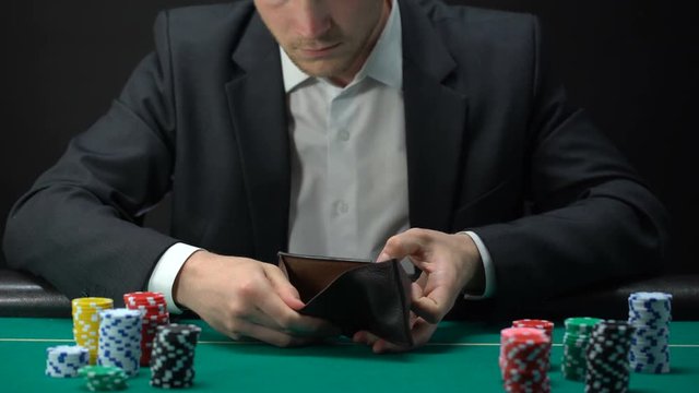 Upset gambler looking in empty wallet, loser at casino table, game addiction
