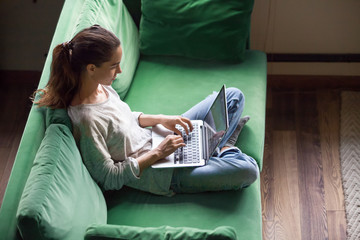 Relaxed woman using laptop sitting on sofa, millennial girl checking news in social networks,...