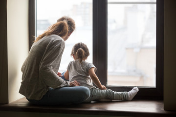 Rear view at kid daughter and single mother sitting on sill dreaming of good future concept,...