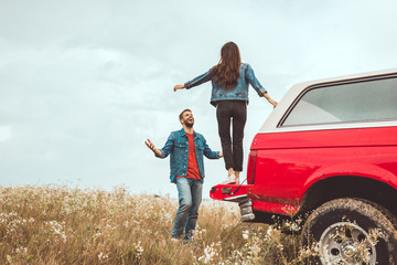 young woman reading to jump from car trunk to her boyfriend in flower field © LIGHTFIELD STUDIOS