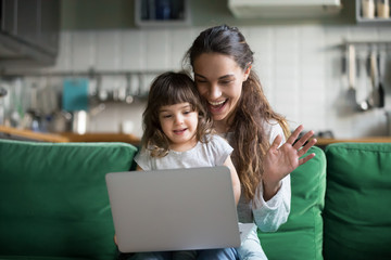 Happy mother and kid daughter waving hands looking at web camera using laptop for video call,...