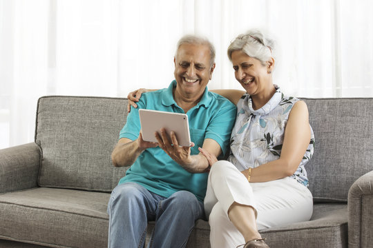 Senior couple sitting on sofa using digital tablet
