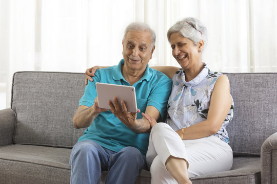 Senior couple using digital tablet sitting on sofa 