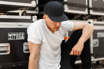 Fashion young man in a fashionable black cap with a stylish white t-shirt sitting near the boxes