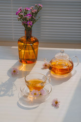 cup of tea on a tray and twigs with flowers on a table near a window of a summer sunny morning