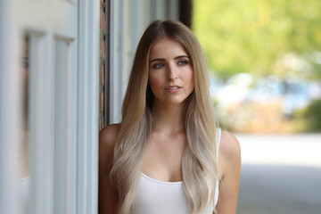 H&uuml;bsche junge Frau steht im Freien an eine Wand gelehnt und schaut in eine Richtung 