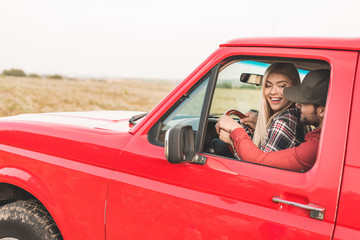 happy young couple sitting on drivers seat together and driving truck by field