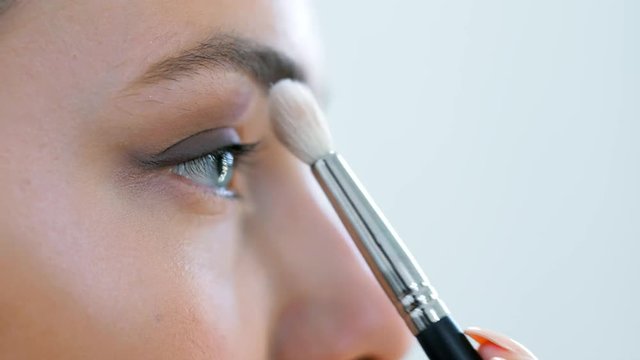 Extreme close up visagiste applying eye shadows using cosmetic brush to face teenage model