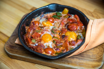Shakshuka - eggs in tomato sauce in a skillet over wooden background.