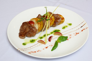 Barbecue with greenery, sauce and lobules of plum on a white dish.