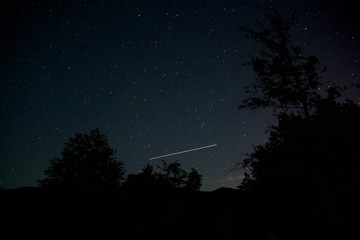 Meteors in the pure starry night sky above the mountain river. Bright multicolored stars of the...
