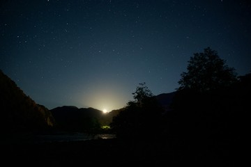 The moon over mountains at night. Wide valley of the river.