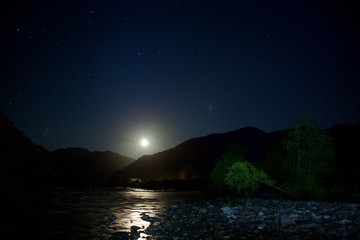 Fototapeta na wymiar The moon over mountains at night. Wide valley of the river.