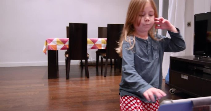 four years blonde cute child watching tablet, singing and dancing on wooden parquet floor of at living room home indoor
