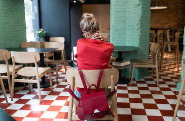 Vintage blonde girl with a bow and red shirt using her phone while smile in a coffee bar