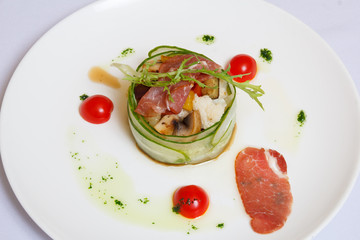 Fried meat and lard, mashed potatoes, decorated by greenery in the cup, made out of the cut cucumbers on a white dish in surroundings the lobules of tomatoes, piece of meat and sauce.