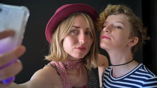 Two young female best friends taking selfie and smiling, isolated on black background