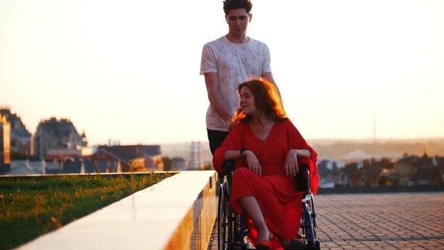 Guy Rolls A Disabled Beautiful Girl In A Wheelchair Outdoors