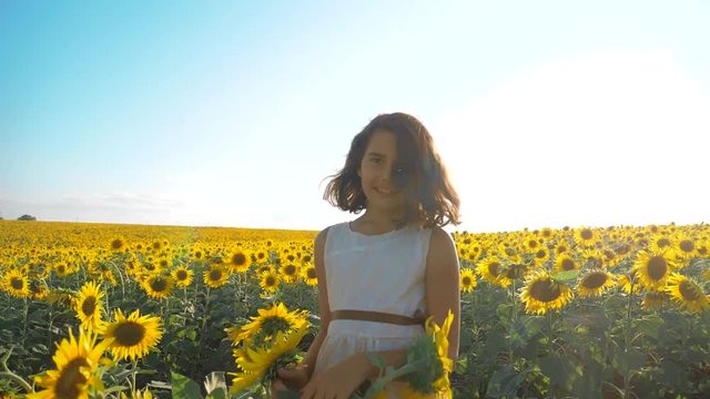 Happy little girl running happy free across the field with sunflowers. slow motion video. smelling big sunflower on summer field. Delight of a pleasant smell. Summer holiday. concept happiness