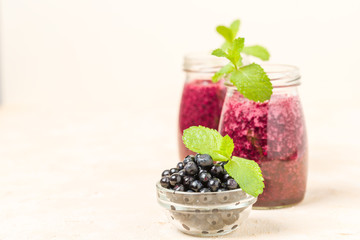 Blueberry smoothie decorated with fresh green mint leaves and raw ripe berries on yellow pastel background.