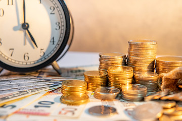 Table clock and gold coin stack on the table with international banknotes currency. Time investment and passing time. Urgency countdown timer for business deadline concept