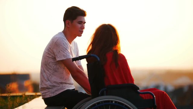 Girl With Red Hair Is Sitting In A Wheelchair And Boyfriend is Sitting With Her, They Talk About Something And Look Into The Distance