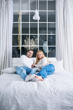 A beautiful happy young couple laying on the bed with christmas lights in the background.
