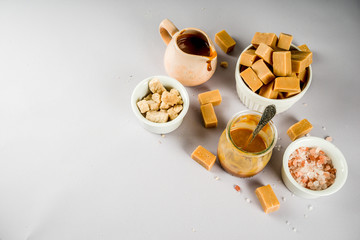 Obraz na płótnie Canvas Salted caramel sauce with fudge candy, fleur de sel, brown cane sugar, grey background copy space top view