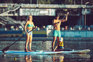 positive smiling boy in rashguard and his young father enjoying stand up paddleboarding