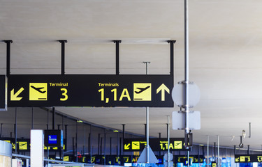 Typical information sign boards with arrows, arrival and departure icons, terminal numbers on airport building's ceiling