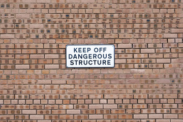 Keep off dangerous structure sign on plain orange brick wall