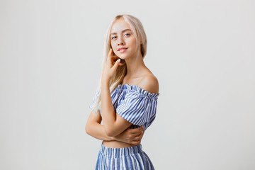 Naklejka premium Calm and friendly beautiful blonde girl in summer outfit is smiling posing at camera, over white background. Emotions, gestures and facial expression