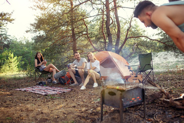Party, camping of men and women group at forest. They relaxing, singing a song and cooking barbecue against green grass. The vacation, summer, adventure, lifestyle, picnic concept