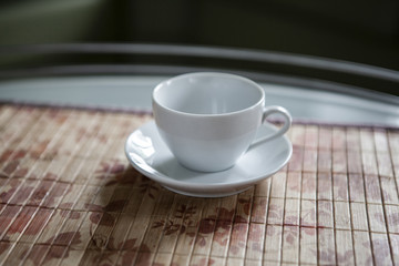 An empty white cup and a saucer stand on a coffee table.