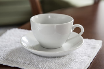 An empty white cup and a saucer stand on a wooden table.