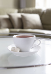 A white cup of tea and a saucer is on a coffee table.