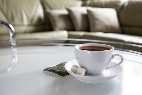 A white cup of tea and a saucer is on a coffee table.