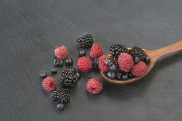 A lot of berries raspberries, blackberries and blueberries poured from a wooden spoon on a black background.