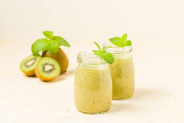 Obraz na płótnie Canvas Kiwi smoothie decorated with fresh green mint leaves and raw ripe cut fruit on yellow pastel background.