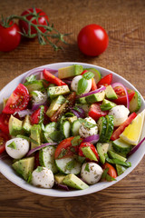 Avocado, tomato, cucumber salad with mozzarella cheese in white bowl on wooden table. vertical