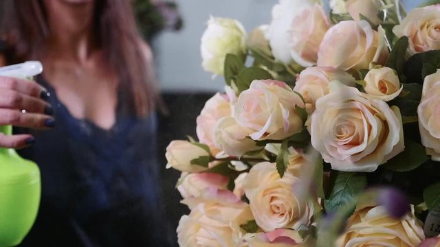 Young female florist spraying water on bunch of flowers in flower shop, close-up