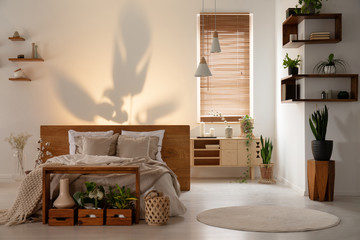 Shadow on the wall above a bed in a modern bedroom interior with wooden shelves, boxes and plants....