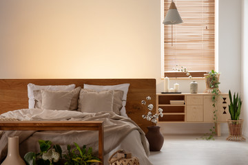 Empty wall in a bedroom interior with a double bed, pillows, cabinet and window blinds. Real photo